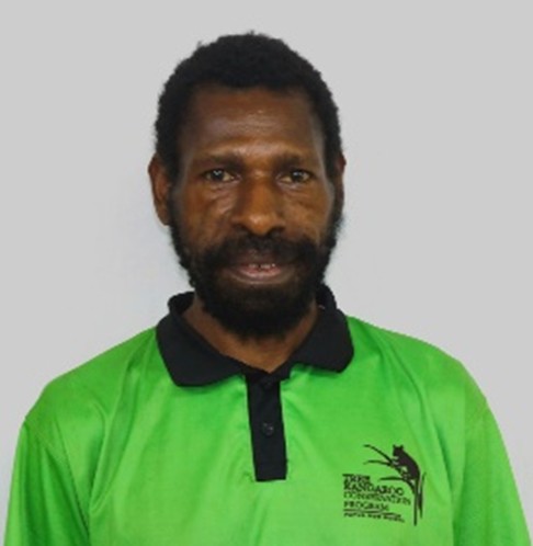 Gunda Domago. A man with short curly hair and a beard wears a bright green collared shirt with the TKCP logo on the chest, standing against a plain light gray background.
