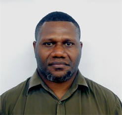 Patrick Vuet. A man with short black hair and a beard wears an olive green collared shirt and looks directly at the camera against a plain white background.
