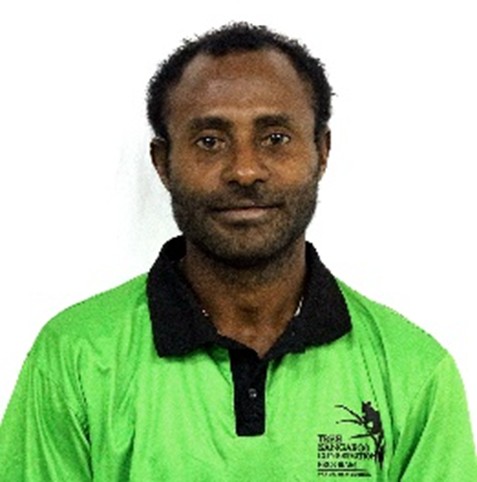 Sisinu Noma. A man with short, curly hair and a trimmed beard is wearing a bright green collared shirt with a black collar, standing against a plain white background.