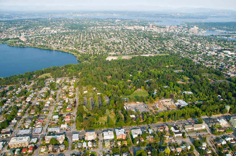 Aerial view of a cityscape with Woodland Park Zoo, residential neighborhoods, a lake on the left, and an urban area spreading toward the horizon under a clear sky.