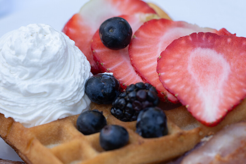 A close-up of a waffle topped with whipped cream, fresh strawberries, blueberries, and a blackberry.